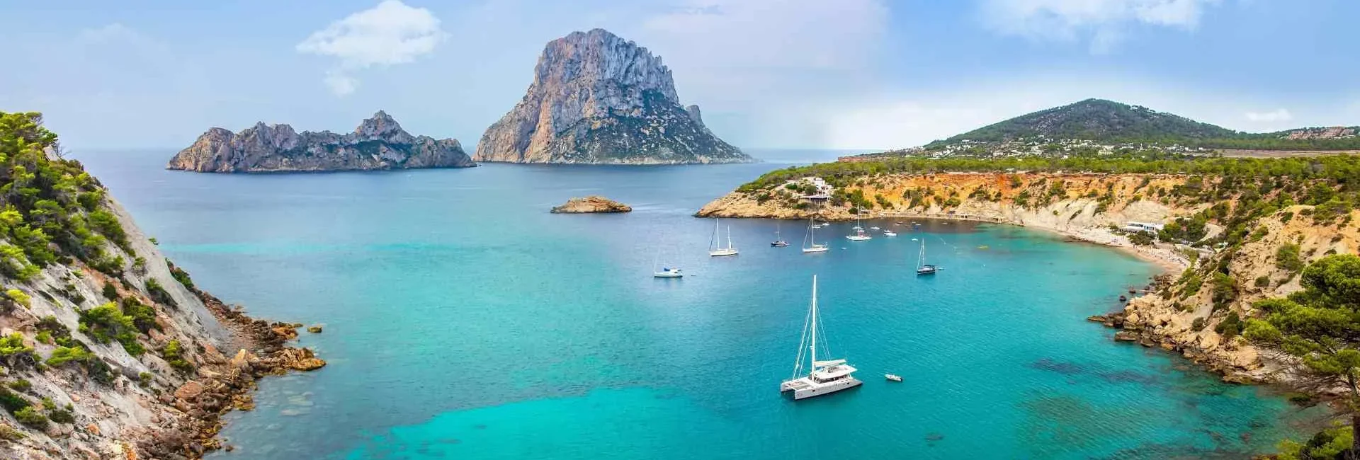 Panoramic views of the Mediterranean and Es Vedrà from Ibiza, with sailboats and yachts anchored in the bay, a scene typical of Europe's most luxurious vacation destinations.