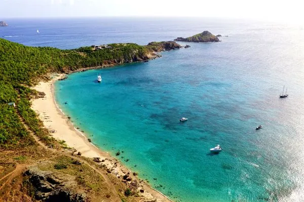 St. Barthélemy's untamed white-sand beach bordered by turquoise Caribbean waters and surrounded by lush green hills, one of the world's most luxurious vacation destinations.