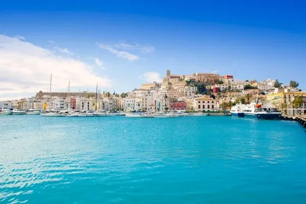 View from the sea of a luxury villa in Ibiza with the harbor in the background, illustrating one of the Mediterranean's most luxurious vacation destinations.