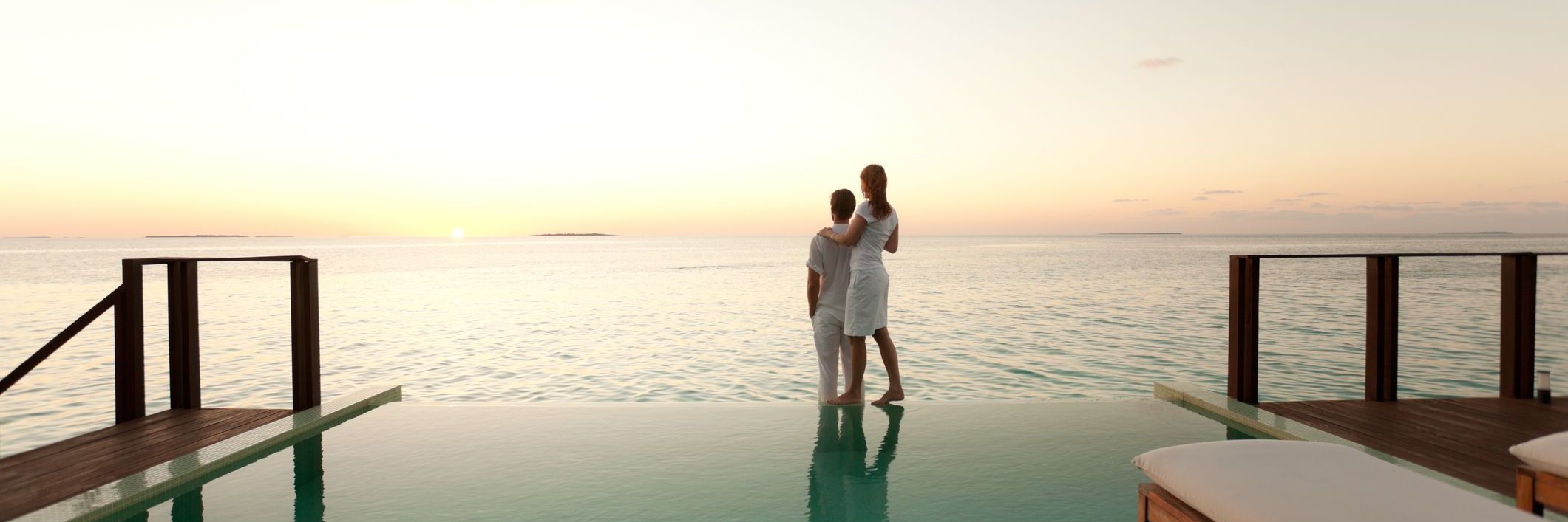 couple enjoying sunset over sea on poolside of overwater bungalow