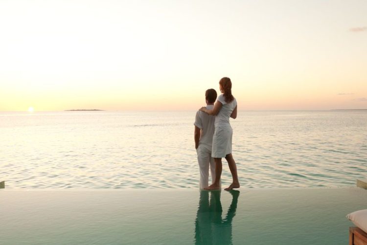 couple enjoying sunset over sea on poolside of overwater bungalow